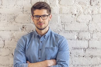 Ein Marketing-Mitarbeiter steht mit verschränkten Armen vor einer Wand.