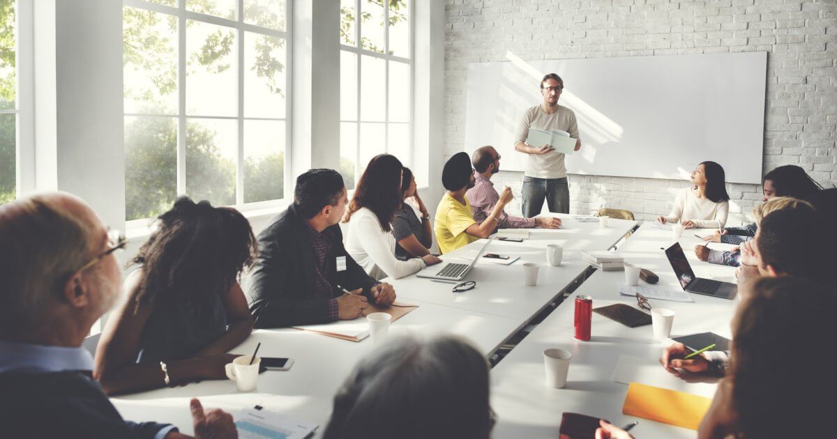 Teilnehmer einer Weiterbildung blicken zu ihrem Dozenten an der Tafel