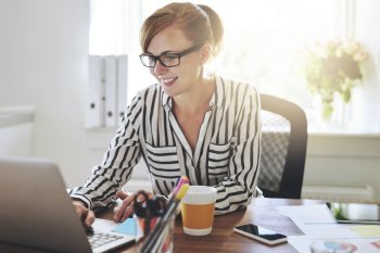 Eine Studentin sitzt an ihrem Schreibtisch und blickt auf ihren Laptop.