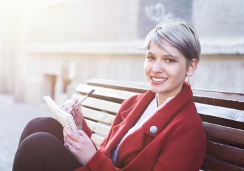 Studentin sitzt auf einer Bank und hat Block und Stift in der Hand.