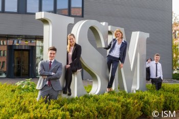 Studierende des ISM stehen vor einer Statue in Gestalt des ISM Schriftzugs